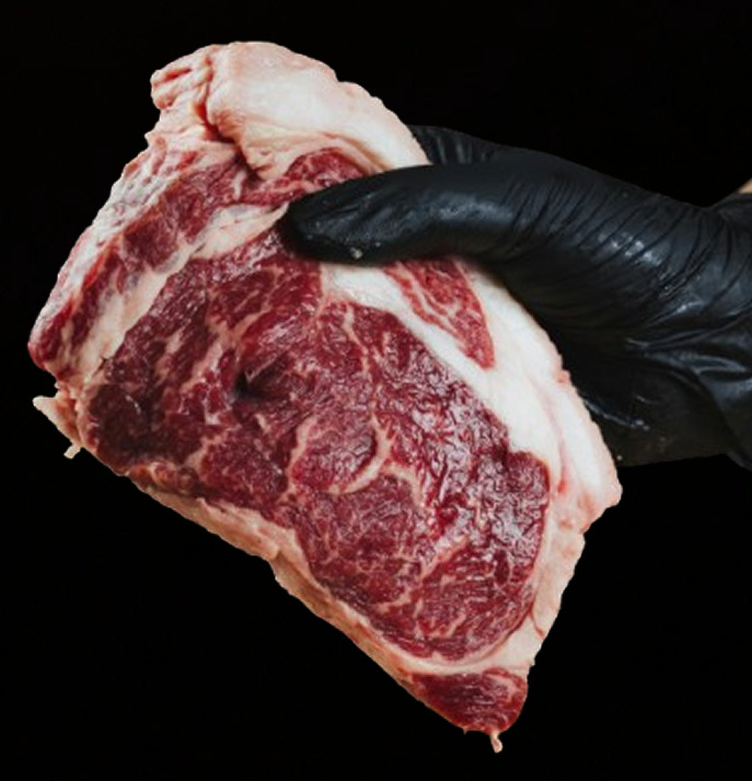 Hand holding a raw marbled steak against a black background.